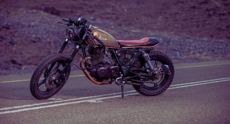 Café racer au réservoir patiné et selle rouge sur une route désertique