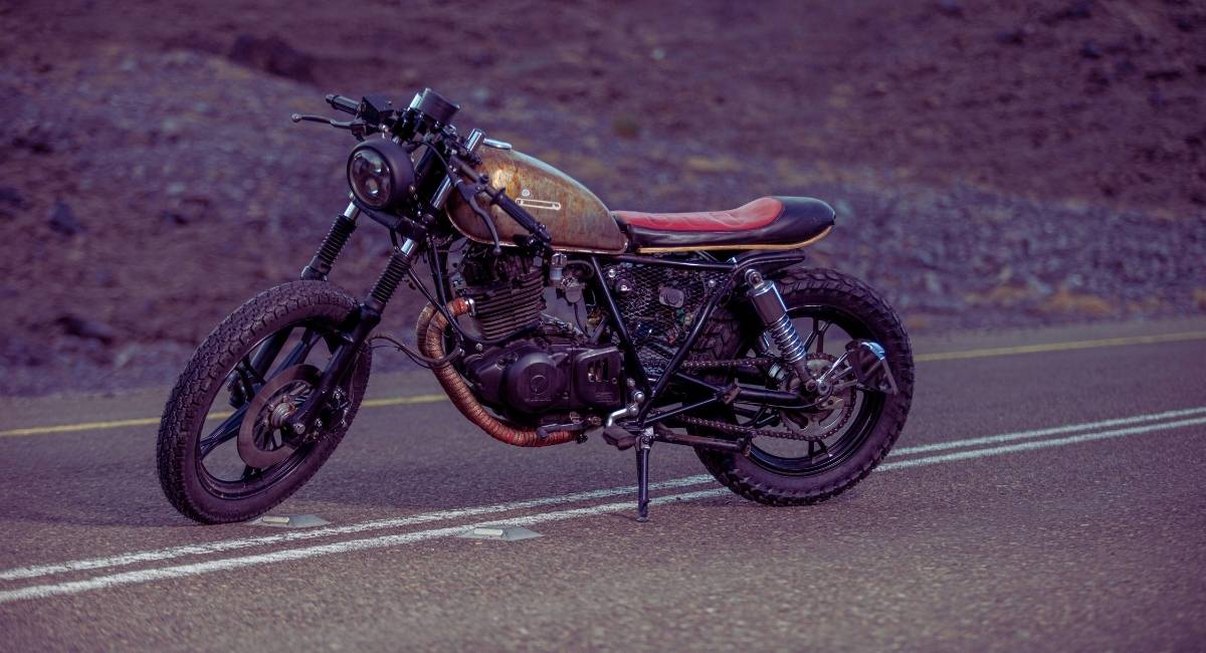Café racer au réservoir patiné et selle rouge sur une route désertique