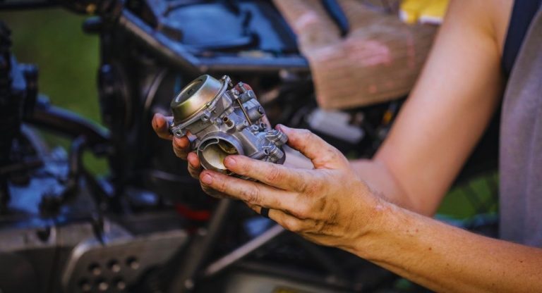 Mains de mécanicien tenant un carburateur de moto démonté
