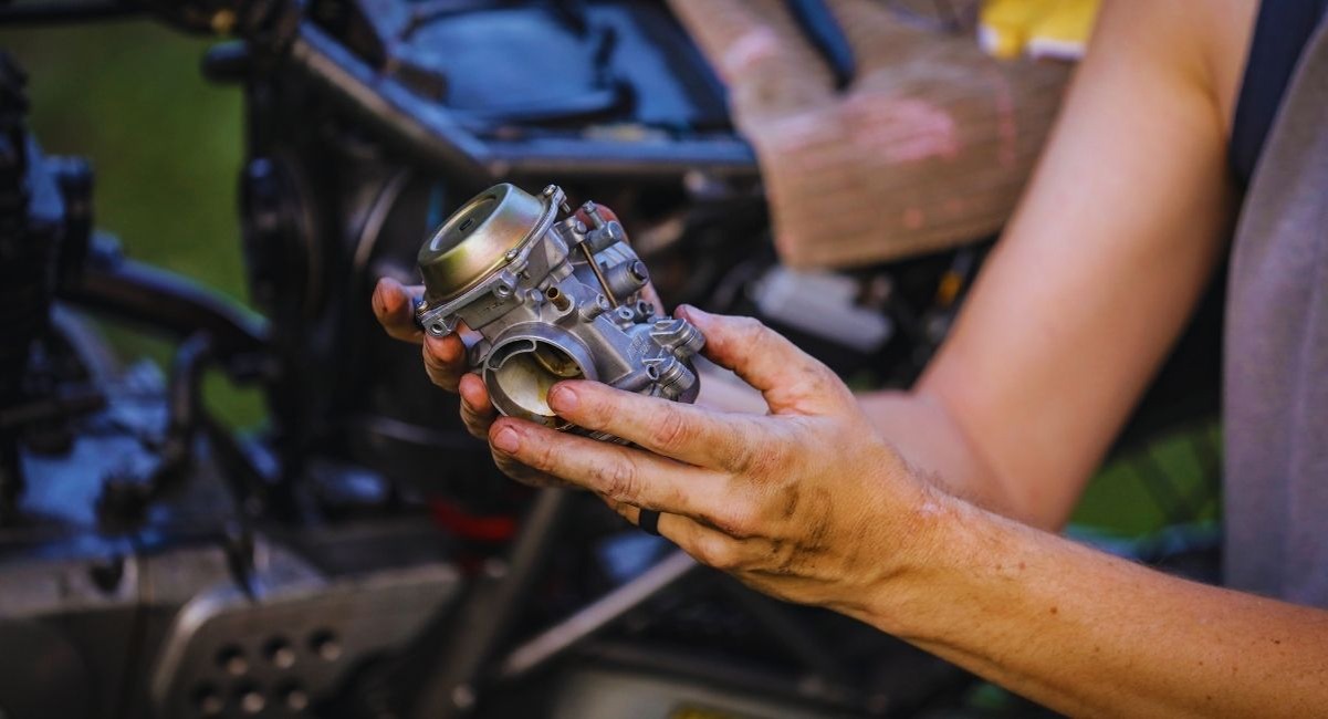 Mains de mécanicien tenant un carburateur de moto démonté