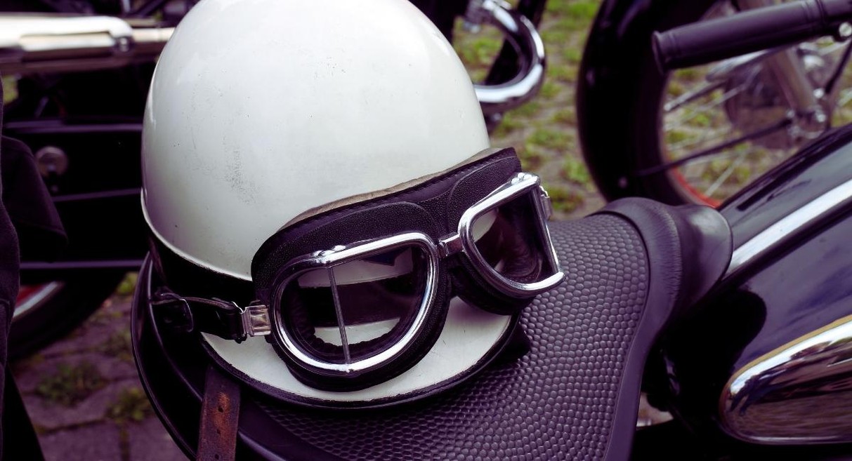 Casque bol blanc et lunettes moto vintage posés sur la selle d'une moto ancienne