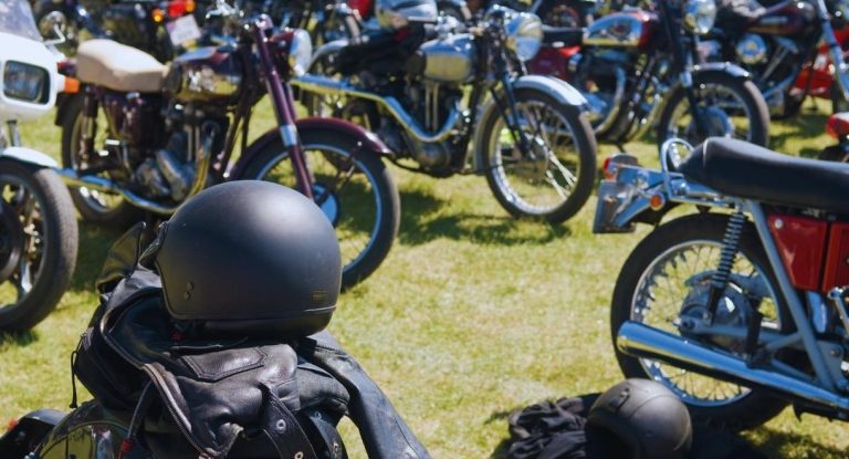 Motos anciennes exposées sur l'herbe lors d'un rassemblement avec casque et blouson au premier plan