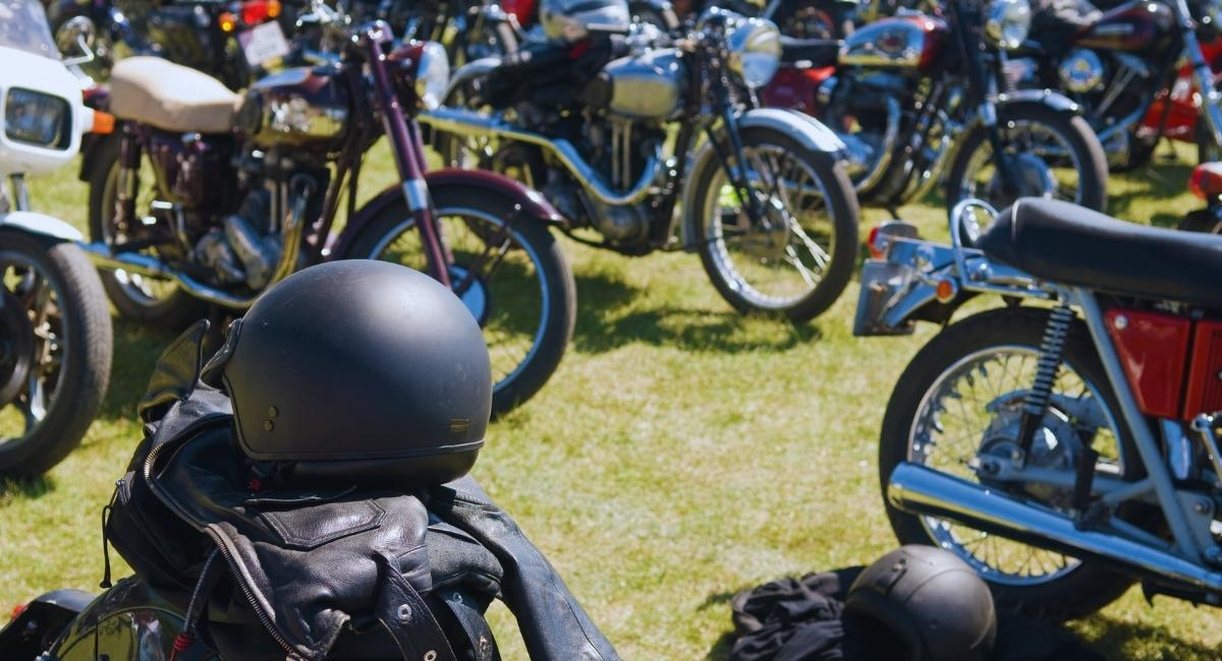 Motos anciennes exposées sur l'herbe lors d'un rassemblement avec casque et blouson au premier plan