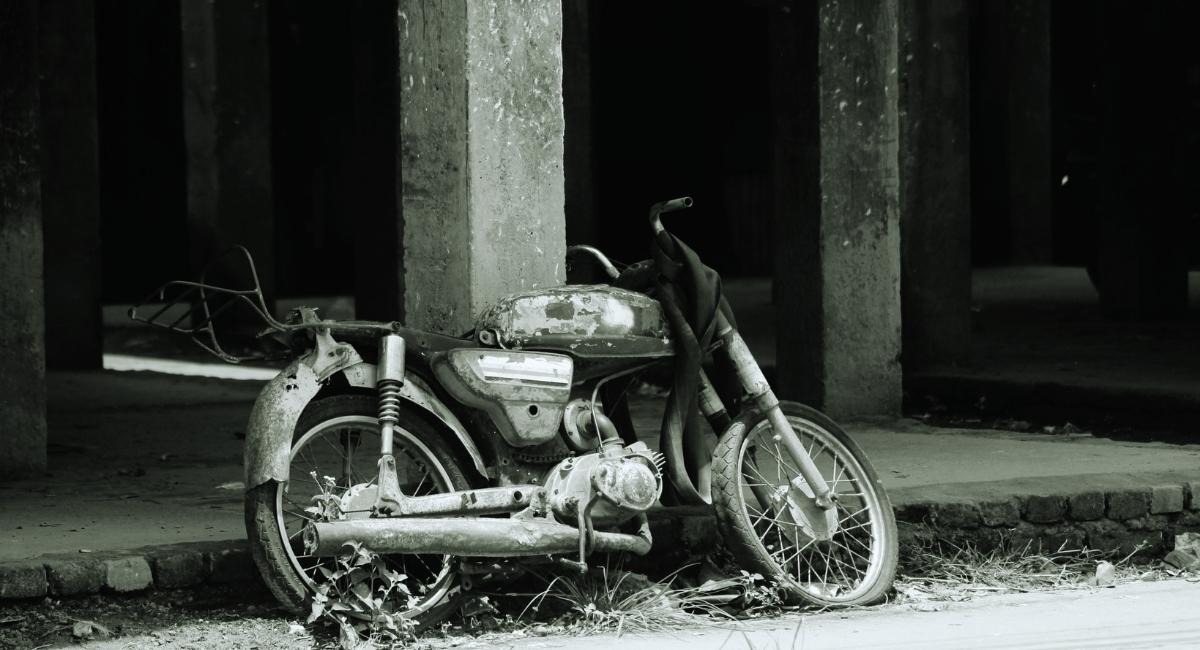 Vieille moto rouillée abandonnée sous un bâtiment en béton