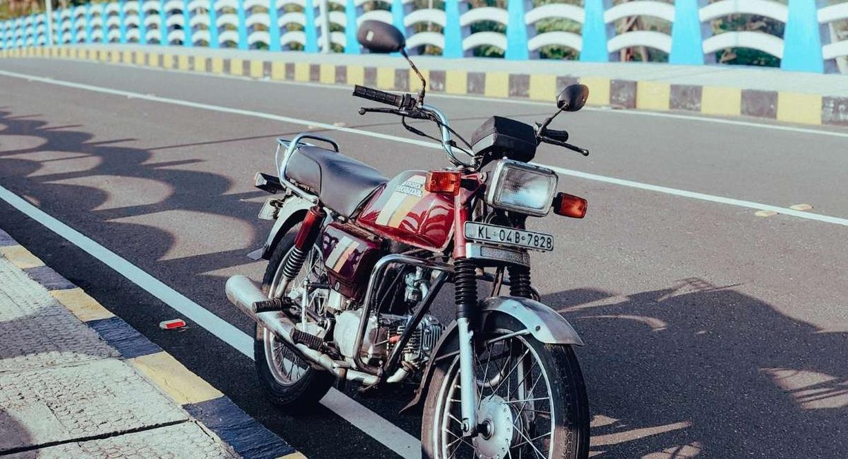Petite moto ancienne rouge garée au bord d'une route ensoleillée