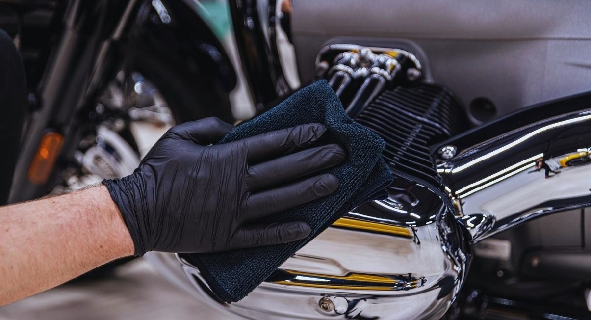 Main gantée nettoyant les chromes d'un moteur de moto avec une microfibre